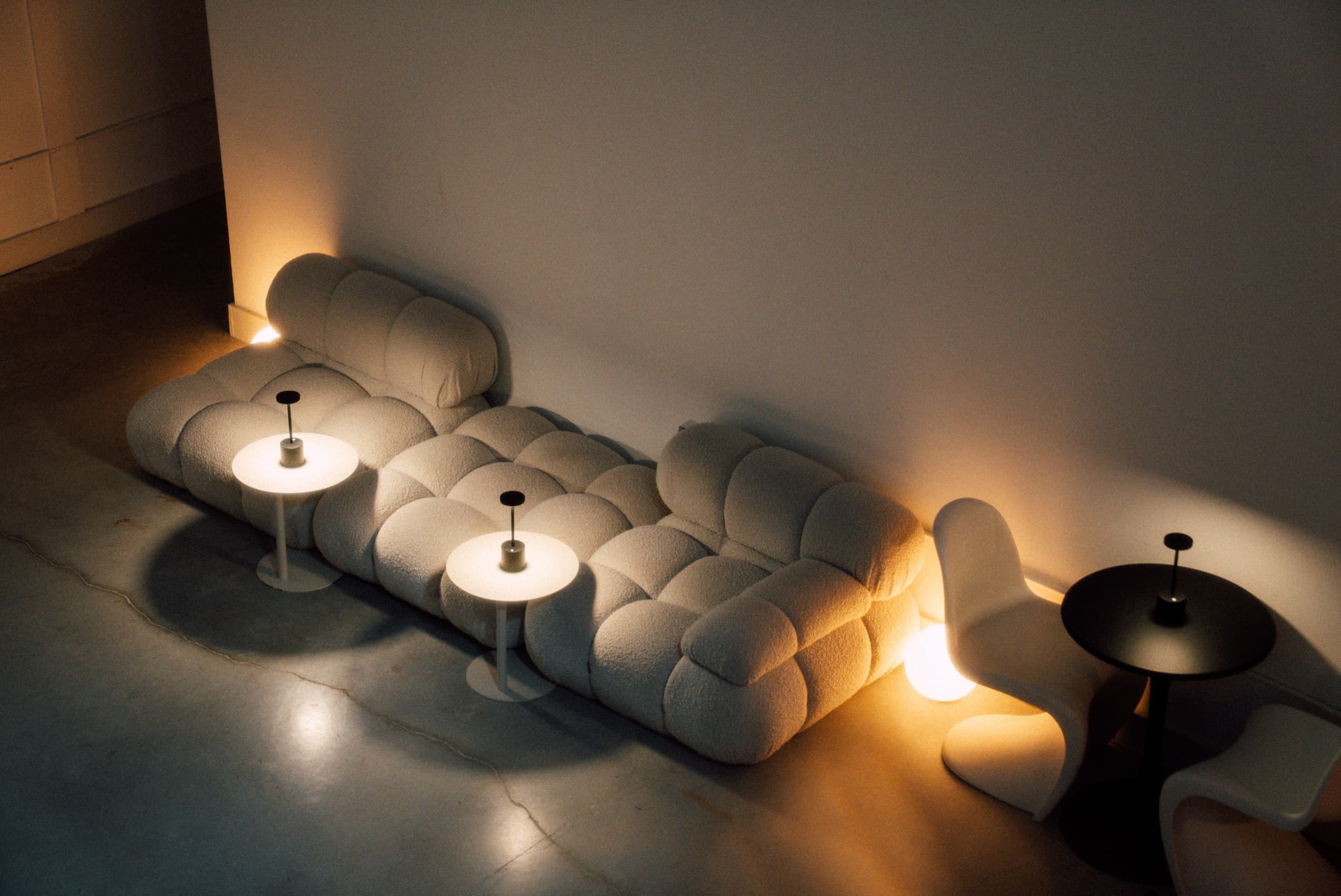 A low bouclé bench lit by two small table lamps against a bare wall.